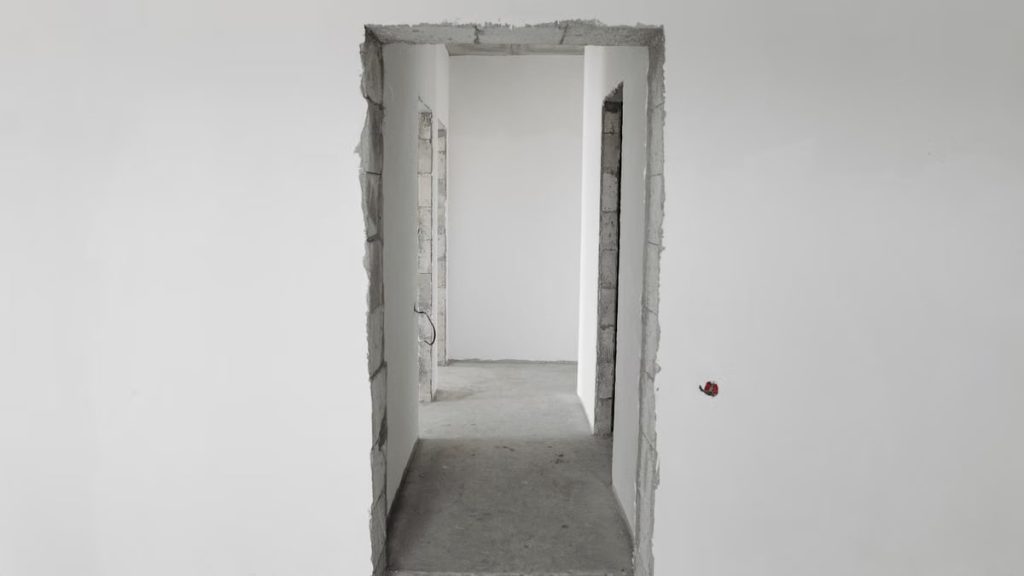 Interior view of a simple white corridor in an unfinished building, showing raw construction details.