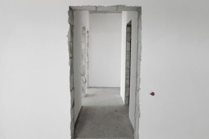 Interior view of a simple white corridor in an unfinished building, showing raw construction details.