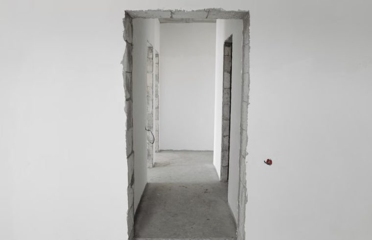 Interior view of a simple white corridor in an unfinished building, showing raw construction details.
